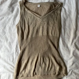 Beige glittrig topp - Snygg beige topp med glittrig finish och v-ringning. Toppen har ribbad midja som ger en schysst passform och markerar siluetten. 
