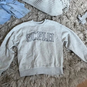 Grå sweatshirt från Gina Tricot XS - Grå sweatshirt från Gina Tricot i storlek XS med SCFLH-tryck i mörkblå på bröstet. Tröjan har rund hals, ribbade muddar och är tillverkad i mjuk bomullsblandning. 