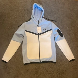 Nike blå och vit vindjacka med luva  - Nike vindjacka i ljusblått och vitt med en dragkedja 