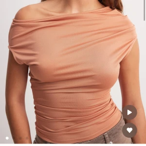 Peachfärgad offshoulder topp - Trendig peachfärgad topp med offshoulder-design och tight passform. Tunt, stretchigt material som sitter snyggt och markerar midjan. Perfekt för dig som gillar en stilren och modern look. Använd 2 gånger, som ny!