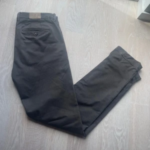 Svarta chinos från Jacob Cohen - Snygga svarta chinos från Jacob Cohen i bomull med klassisk passform. Byxorna har dragkedja, knappstängning och diskreta fickor fram och bak. Insidan är dekorerad med blommigt mönster och citat. Perfekta för en clean och stilren look.