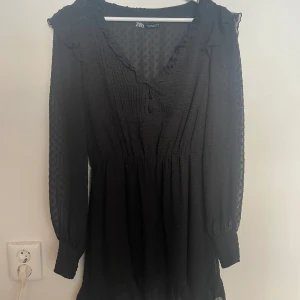 Svart prickig kortklänning från Zara - Supersöt svart kortklänning från Zara med diskret prickigt mönster, v-ringning och volangdetaljer vid axlar och hals. Långa ärmar med smock vid handlederna och markerad midja. Perfekt för dig som gillar en feminin och trendig look. Strl s. Använt några gånger 