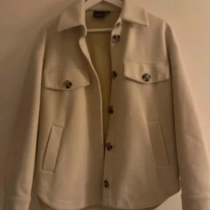 Beige overshirt med stora knappar - Stilren beige overshirt/höstjacka från vero Moda med stora bruna knappar framtill och två bröstfickor med lock. Jackan har klassisk krage, raka ärmar och är tillverkad i ett mjukt ullblandat material. Perfekt för lager-på-lager under hösten!🩷