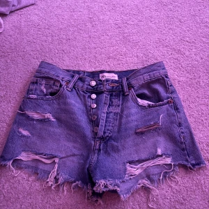 Blå slitna jeansshorts från Zara - Snygga blå jeansshorts från Zara med hög midja, slitna detaljer och fransig kant. Knappar framtill och klassisk femficksmodell. Perfekta för en chill sommarlook.