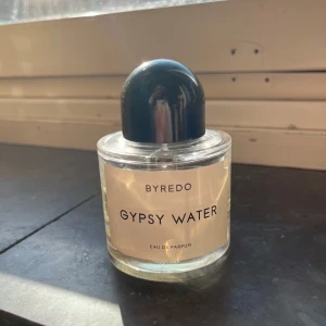 Byredo Gypsy Water 100ml parfym - Lite mer än hälften är kvar. Byredo Gypsy Water Eau de Parfum i en stilren, rund glasflaska med svart rund kork. Flaskan rymmer 100 ml och har en minimalistisk vit etikett med svart text. Parfymen är ljusgul och flaskan är tillverkad i glas.