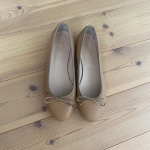 Beige ballerinaskor med rosett - Snygga beige ballerinaskor från a pair. Skorna har rund tå, platt sula och en söt rosett framtill. Made in Italy