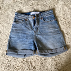 Ljusblå jeansshorts från Amisu - Snygga ljusblå jeansshorts från Amisu med klassisk femficksdesign och uppvikta benslut. Shortsen har hög midja och gylf med dragkedja och knapp. Perfekta för varma dagar och enkla att matcha med allt. 🥰