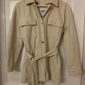 Beige kappa i jeanstyg från Zara  - Snygg beige kappa i jeanstyg från Zara, med knappar och snörning i midjan. 