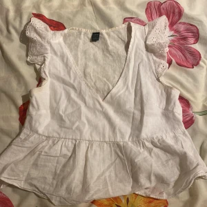 Vit blus med spetsvolang från SHEIN - Supersöt vit blus från SHEIN i storlek S med v-ringning och volang nedtill. Ärmlös modell med spetsdetaljer på axlarna som ger en romantisk vibe. Luftigt material som känns lätt och fräscht, perfekt för varma dagar. Passar dig som gillar en feminin och chill stil.