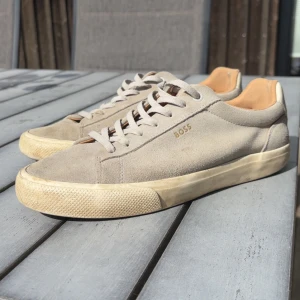 Gråa Hugo boss mocka skor - Säljer ett par stilrena gråa Hugo boss skor med klassisk snörning och platt sula. Skorna har en rund tå och är perfekta för dig som gillar en clean och enkel look. Passar till jeans och streetwear för en avslappnad vibe.