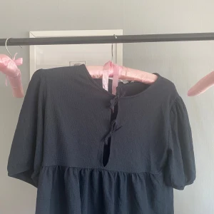 Svart kortärmad blus med snörning från Lager 157 - Supersöt svart blus från Lager 157 med puffiga kortärmar. Blusen har en cool snörningsdetalj framtill vid halsen och är gjord i ett mjukt, strukturerat material som känns skönt mot huden. Prislappen är kvar. Denna är lite stor i storleken så om du har någon större storlek än 150 går de bra ändå.