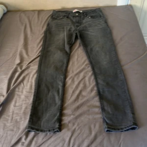 Levi's 512 Slim Taper grå jeans - Säljer ett par Levi's 512 Slim Taper jeans i mörkgrå färg. Modellen har smal passform med avsmalnande ben och klassiska fem fickor. Materialet är en mix av bomull, polyester och elastan för extra komfort och stretch. Perfekt för dig som gillar en modern och clean look.