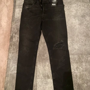 Svarta tapered jeans från Diesel  - Svarta Diesel  jeans med tapered passform och stretch. Snyggt slitna, klassisk femficksmodell och knappgylf. Perfekta för dig som gillar streetstyle och vill ha bekväma jeans med attityd. Vid fler frågor kom DM🔥