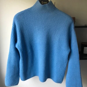 Blå ribbad polotröja från H&M - Säljer en blå polotröja från H&M i storlek S. Tröjan är ribbstickad med hög krage och har långa ärmar med slits vid ärmslutet. Perfekt för dig som gillar en chill och stilren look under höst och vinter.
