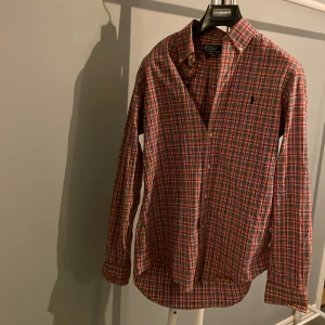 Rutig skjorta från Polo Ralph Lauren - Säljer en rutig skjorta från Polo Ralph Lauren i custom fit. Skjortan har en klassisk krage, långa ärmar och knappar framtill. Färgerna är röd, vit, blå och gul, och materialet är mjuk bomull. Perfekt för dig som gillar en chill och stilren look. Hör av er vid funderingar🤗