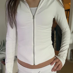 Vit zip hoodie från Nelly XXS - Slutsåld vit hoodie från Nelly med hel dragkedja framtill och ribbad nederkant. Storlek xxs.