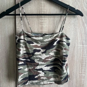 Camouflage linnetopp med smala band från Ginatricot - Snygg linnetopp med camouflage-mönster i grönt, beige, brunt och svart. Modellen är croppad med smala axelband och har en rak, enkel form. Perfekt för dig som gillar streetstyle och vill sticka ut med coola mönster.