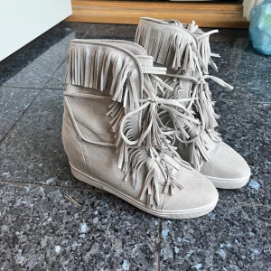 Gråa mocka boots med fransar från Siader - Säljer ett par gråa boots med klack från Siader i mjuk mocka med coola fransdetaljer och snörning framtill. Skorna har en dold kilklack och platt sula💕