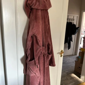 Rosa frottérock med huva från Rituals - Mysig rosa rock från Rituals i mjuk frotté, perfekt att chilla i hemma. Den har stor huva, två rejäla fickor och bälte i midjan för extra comfort. Snygg och enkel design som ger skön vibe efter duschen eller när du bara vill slappa.        Finns även ute på annan marknasplats, först till kvarn gäller.