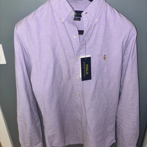 Ljuslila skjorta från Polo Ralph Lauren - Slim fit stretch oxfordskjorta i ljuslila från Polo Ralph Lauren. Klassisk button-down krage, broderad logga på bröstet och knappar framtill. Skjortan är gjord i bomull med stretch för extra komfort. OBS endast testad!! Storlek S/m. priset är diskuterbart