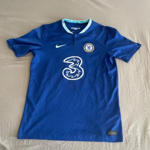 Chelsea FC matchtröja James #24 Nike XL - Chelsea FC matchtröja i blått med vit logga och detaljer, tillverkad i Dri-FIT material för bästa komfort. Framsidan har klubbmärke och sponsortryck, baksidan har JAMES och nummer 24 i vitt. Rund hals med mönstrad insida och korta ärmar.