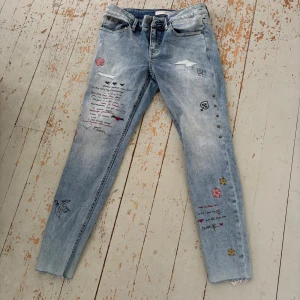 Odd Molly ljusblå jeans med broderier - Säljer ett par ljusblå jeans från Odd Molly med snygga broderade detaljer, text och stjärnor på benen. Modellen är slim och har dragkedjor vid bensluten samt klassisk femficksdesign. Perfekt för dig som vill ha jeans med unik stil och coola detaljer.