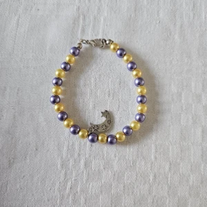 Lila och gul pärlarmband med månhänge - Superfint armband med pärlor i lila och gul, och ett silverfärgat hänge i form av en måne med små stjärnor. Lås i metall och pärlorna har en snygg glansig finish.