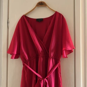 Röd omlottklänning med volang - Snygg röd kortklänning från Bubbleroom med omlott-design och v-ringning. Klänningen har luftiga korta ärmar, knytband i midjan och volangdetalj längst ner. Materialet är mjukt och lätt, perfekt för varma dagar. Passformen är normal och ger en skön siluett.