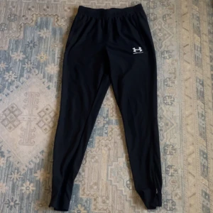 Helt nya svarta under armour byxor  passar S/M - Svarta träningsbyxor från Under Armour med vit logga på höften. Byxorna har elastisk midja och smal passform som sitter snyggt längs benen. Perfekta för gymmet eller löprundan, tillverkade i mjukt syntetmaterial som andas och ger bra rörelsefrihet.