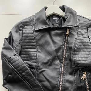 Svart skinnjacka från Boohoo - Snygg svart skinnjacka från Boohoo med coola quiltade detaljer på axlar och ärmar. Jackan har en croppad passform, silverfärgade dragkedjor och bred krage. Perfekt för dig som vill ha en edgy look med street-vibe.