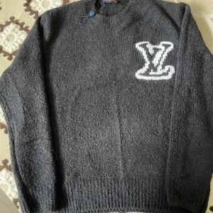 Svart stickad Louis Vuitton tröja storlek m fast det står xs - Svart stickad tröja från Louis Vuitton i storlek m. Tröjan har ett stort vitt LV-logo broderat på bröstet och rund hals. Materialet är grovstickat och känns riktigt lyxigt. Perfekt för dig som vill ha en statement piece med designer-vibe.