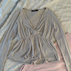 Ljusgrå topp - Supersöt ljusgrå topp från Bik Bok med v-ringning och en fin rosettdetalj framtill. Toppen har lång ärm och ett flowigt fall nedtill.💖