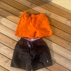 Svarta och orange badshorts Polo Ralph Lauren 200kr st  - Två par badshorts från Polo Ralph Lauren, ett par i svart och ett par i knallorange. Båda har elastisk midja, meshfoder och klassisk Polo-logga broderad framtill. Perfekta för stranden eller poolen, riktigt snygga färger och stilren design.