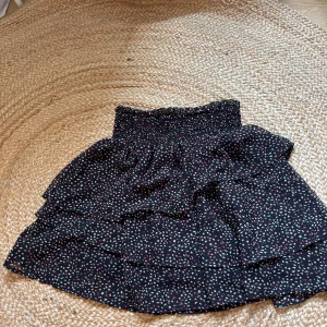 Svart volangkjol med prickigt mönster H&M - Supersöt svart kortkjol från H&M med volanger och prickigt mönster i vitt och rosa. Kjolen har smockad midja som sitter bekvämt och ger en snygg siluett. Perfekt att matcha med en enkel topp och sneakers för en chill look. Pris går att diskutera 💗💗