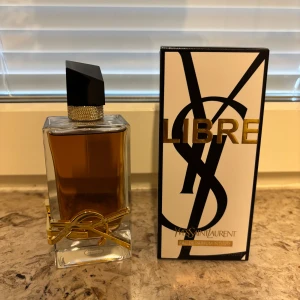 Yves Saint Laurent Libre Eau de Parfum - Säljer en lyxig parfym, Libre Eau de Parfum Intense från Yves Saint Laurent. Flaskan är rektangulär i klart glas med gyllene YSL-logga och svart asymmetrisk kork. Doften är intensiv och elegant, perfekt för dig som gillar exklusiva parfymer.