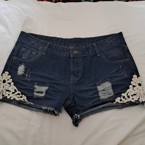 Söt basic Low waist jeans shorts - Söta Low waist jeans shorts. En mörkare nyans av blå med några slitna detaljer och blommig spets vid sidan. Köpt från en marknad i Thailand.