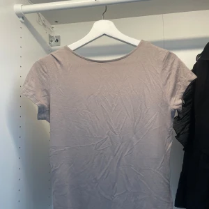 Beige topp med djup rygg från 157 - Snygg beige topp från 157 i storlek M. Modellen har korta ärmar och en riktigt djup, rundad rygg som ger en cool vibe. Materialet är mjukt och stretchigt, perfekt för att matcha med jeans eller kjol. Enkel design utan mönster eller detaljer.