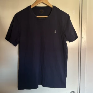 Mörkblå t-shirt från Polo Ralph Lauren/de är bara tagen inne som man ser att den är använd annars ser man att den är ny!  - Snygg mörkblå t-shirt från Polo Ralph Lauren med klassisk rund hals och korta ärmar. T-shirten har det ikoniska broderade Polo-logot på bröstet i vitt. Tillverkad i mjuk bomull för skön känsla och stilren look.