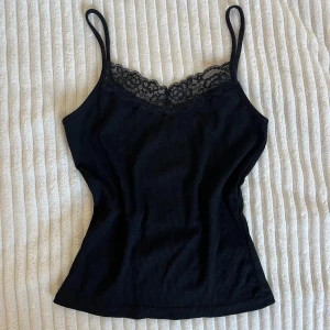Svart ribbad linnetopp med spets - Svart ribbad linnetopp med smala axelband och snygg spetskant vid halsen. Toppen har en figurnära passform och gjord av tjockare och finare material. Vet tyvärr inte vart tröjan är från då etiketten ej är kvar men linnet är superfint så passa på💗