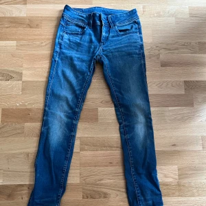 G-Star RAW Lynn Mid Skinny jeans blå 26/30 - Snygga blå jeans från G-Star RAW, modell Lynn Mid Skinny. De har en smal passform, klassisk femficksdesign och medelblå tvätt med lätt slitningar. Midwaist och skinny legs ger en modern look. Perfekta för dig som gillar stilrena och bekväma jeans.