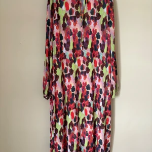 Blommig långklänning från Y.A.S - Säljer en färgstark långklänning från Y.A.S i storlek L. Klänningen har ett blommigt mönster i rött, rosa, grönt och svart med långärmade ärmar och lätt plisserad struktur. 