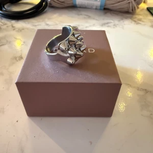 Silvrig ring med nitar från Edblad - Ring i blankt silverfärgat metall från Edblad. Ringen har flera konformade nitar på ovansidan som ger en edgy och unik look. Perfekt för dig som vill addera lite attityd till din stil.