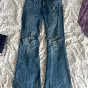 Blå bootcut jeans från g perfect jeans - Säljer ett par blå bootcut jeans från gina i storlek 38. De har slitna detaljer och hål vid knäna för en cool, avslappnad vibe. Klassisk femficksmodell med normal passform och tillverkade i jeansmaterial. Perfekt för dig som gillar retrostil och lite edge. !uppsprättade där nere!