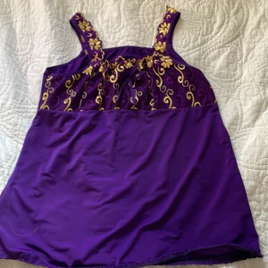 Lila linne med broderi - Superfint lila linne med breda axelband och detaljerat gult broderi med blommor och snirkliga mönster upptill. Linnet har en rak passform och ärmlös design, perfekt för dig som gillar färg och unika detaljer. Materialet känns mjukt och lätt mot huden.