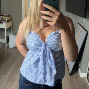 Blåvit randig bandage topp med knyt - Superfin bandeau topp med blåvita ränder och en stor knytning framtill. Sitter snyggt axelbandslöst och har en lätt v-ringad form. Perfekt för varma dagar och ger en fräsch sommarkänsla. Passar dig som gillar en chill och trendig stil. Stl s men passar även m