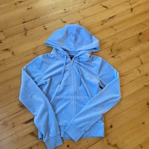 Ljusblå velour hoodie Juicy Couture XS -  Inga defekter! Säljer en ljusblå hoodie från Juicy Couture i mjuk velour med dragkedja och huva. Tröjan har långa ärmar, snörning vid huvan och snygga detaljer i silver med Juicy Couture-logga. Broderad J på bröstet och ribbade muddar. Perfekt för chill dagar.