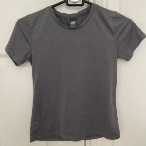 Grå sportig t-shirt från H&M - En grå tränings t-shirt från H&M. Jag har använt den få gånger, på sista bilden ser man att det har suttit en namnlapp men det syns inte när man har det på sig.