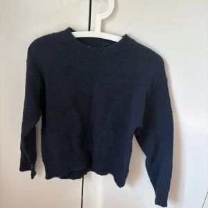 Mörkblå stickad tröja Gina Tricot - Mysig mörkblå stickad tröja från Gina Tricot med rund hals och långa ärmar. Tröjan har en enkel, klassisk design och är perfekt för att hålla sig varm under kyliga dagar. Materialet är mjukt och skönt mot huden.