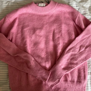Rosa stickad tröja från H&M - Mysig rosa stickad tröja från H&M med rund hals och ribbade muddar vid ärmslut och nederkant. Perfekt för att addera lite färg till din garderob. Långärmad och i en skön, mjuk kvalitet som passar när det är lite kyligare ute.