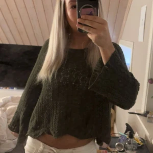 Mörkgrön stickad croppad tröja - Säljer en mörkgrön stickad tröja med croppad passform och vågig nederkant. Tröjan har breda, långärmade ärmar och ett snyggt hålmönster framtill. Perfekt för dig som gillar en chill och trendig stil.